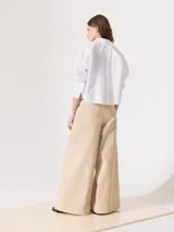 Pantalón de tiro alto color beige, de corte palazzo, con cinturón con hebilla forrada, bolsillos diagonales delanteros y bolsillos sastre traseros.