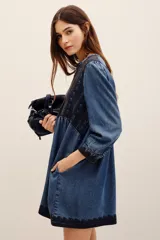 Vestido corto de tencel en color azul, con mangas largas abullonadas y escote en V profundo. Cuenta con detalles de bordados oscuros en el pecho, los puños y el ruedo, y una falda de corte evasé.