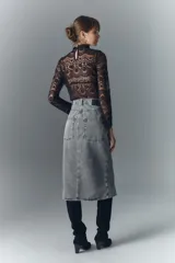 Falda midi de denim rígido con lavado gris, presenta cierre frontal con botones metálicos grabados y diseño de recortes verticales en el frente.