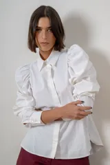 Camisa de algodón color marrón con mangas largas abullonadas, cuello clásico y cierre frontal oculto. Presenta botones decorativos con strass en los puños y en el cuello.