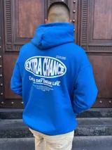 Canguro oversize de color azul vibrante, con capucha y estampado gráfico en la espalda que incluye el texto 'EXTRA CHANCE' y frases motivacionales en color blanco.