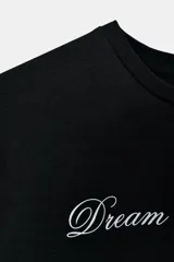 Camiseta blanca de manga corta y cuello redondo, con estampado en tipografía cursiva negra que dice "Creativity doesn't sleep" en diagonal.