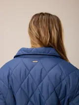 Campera acolchada de diseño matelassé con patrón de rombos, color bordó. Presenta cuello camisero, cierre frontal con cremallera metálica, cintura entallada con elástico y bolsillos laterales. Incluye un pequeño bordado distintivo en el pecho.