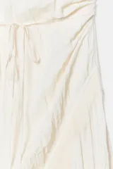 Vestido midi lencero de color blanco, confeccionado en tejido con efecto arrugado. Cuenta con escote recto, tirantes finos ajustables, diseño cruzado con cinturón fino para anudar y detalles de encaje en los acabados de la falda.