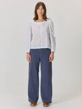 Camisa blanca de algodón con mangas largas abullonadas, detalle de volados en los hombros y puños elásticos. Presenta un diseño con cuello redondo y corte holgado.