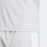 Remera deportiva Adidas Tiro26 League, color gris claro, de manga corta y cuello redondo. Presenta paneles blancos en los hombros y tres franjas blancas en los hombros. Incluye logo Adidas en el pecho.