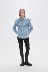 Camisa celeste de jean con cuello clásico, cierre frontal con botones y volados en el canesú delantero y trasero.