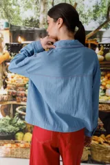 Blusa celeste de denim con cuello polo, manga larga y botones marrones.