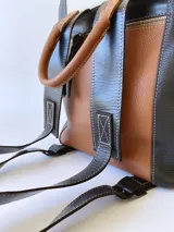 Mochila de cuero tricolor en tonos marrón tostado, negro y blanco, con bolsillo frontal con cierre, tiradores de cuero y detalle de etiqueta con logo grabado.