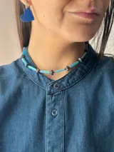 Collar corto de diseño artesanal compuesto por cuentas cilíndricas de vidrio en tono celeste y pequeñas piedras naturales esféricas en tonos azulados, intercaladas con detalles metálicos. Incluye cadena de acero quirúrgico para ajuste de largo.
