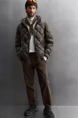 Campera puffer verde oliva acolchada con diseño de rombos, capucha y cierre frontal con cremallera. Incluye bolsillos laterales con cierre. Relleno de plumón y plumas.