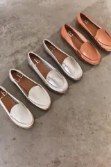 Mocasines de cuero color dorado con acabado texturizado, diseño clásico de punta redondeada y costuras visibles en el empeine. Cuentan con suela plana y flexible.