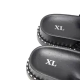 Sandalias de plataforma baja color negro, con dos tiras anchas en el empeine: una frontal lisa y otra trasera de diseño trenzado. La suela cuenta con un detalle de pequeñas tachas metálicas plateadas en todo el contorno.
