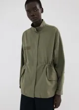 Chaqueta estilo militar verde militar, de diseño oversize, cuello alto, cierre frontal con cremallera y botones ocultos bajo tapeta, bolsillos con solapa y bolsillos de ribete en el pecho.