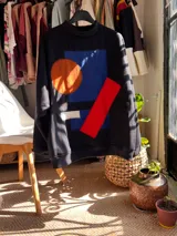 Buzo oversize negro con diseño artesanal de figuras geométricas aplicadas en tela de colores azul, naranja, rojo y blanco.