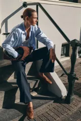 Mocasín plano de piel color marrón, estilo penny loafer con antifaz y detalle metálico dorado. Presenta punta redonda y costuras visibles.