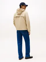 Campera beige de nailon repelente al agua y resistente al viento, con capucha fija, cierre de cremallera, dos bolsillos en la cintura, bolsillo interior con cremallera, puños elásticos con botones a presión, solapa de protección en la parte trasera y parche con el logo de Tommy Hilfiger en la manga.