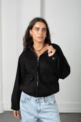Campera de gamuza negra con cierre frontal, cuello camisero, bolsillos delanteros con solapa y puños con botón.