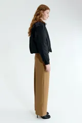 Pantalón sastrero de corte holgado en color tostado, con diseño asimétrico cruzado en la cintura, botón frontal y pliegues en las piernas.