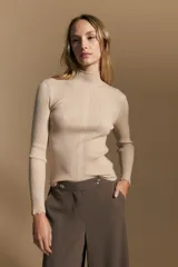 Polera de tejido acanalado color beige, con cuello alto y mangas largas con terminaciones onduladas en los puños. Presenta un ajuste al cuerpo.