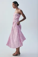 Vestido midi de color rosado con estampado de lunares negros, cuello halter con tirantes finos ajustables, escote recto y diseño fluido con volumen.