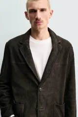 Blazer de corte relajado confeccionada en piel con acabado de ante. Presenta cuello con solapas de muesca, cierre frontal de dos botones, mangas largas y bolsillos de plastrón en la cadera. El diseño no posee forro interior y cuenta con aberturas en la parte trasera.