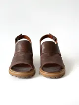 Sandalias de cuero color chocolate con suela track y taco bajo cuadrado. Poseen capellada cerrada con aberturas laterales y tira ajustable en el talón con hebilla metálica.