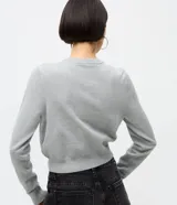 Cardigan corto de punto color gris, con cuello redondo, mangas largas y cierre frontal con botones. Presenta un diseño ajustado al cuerpo con bordados de cerezas distribuidos por toda la prenda.