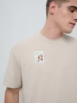Remera de manga corta color beige, con cuello redondo y diseño holgado. Cuenta con un pequeño estampado rectangular en el pecho con motivo futbolero.