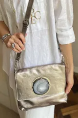 Sobre de cuero metalizado en tono plateado con correa larga ajustable y desmontable. Presenta un aplique circular central con una piedra de ágata natural incrustada.