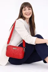 Bandolera de diseño acolchado con costuras geométricas en forma de V, color rojo. Cuenta con doble cierre metálico superior, bolsillo trasero con cierre y correa de cinta ajustable. Incluye placa metálica decorativa en el frente.