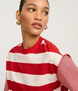 Remera de algodón con cuello redondo, cuerpo a rayas horizontales anchas rojas y blancas, y mangas cortas con rayas horizontales finas rojas y blancas. Presenta sisa desplazada y costuras aparentes.