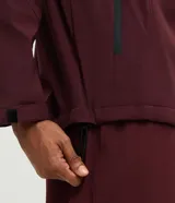 Campera deportiva Get Over de hombre, color bordó, con capucha ajustable, cierre frontal y bolsillos con cremallera. Confeccionada en tejido técnico resistente al agua.