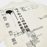 Remera de algodón color blanco hueso con corte oversize, hombros caídos y cuello redondo. Presenta un estampado minimalista en el pecho con tipografía y caracteres asiáticos, y un logo bordado en la manga.