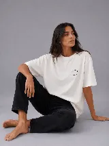 Remera de corte oversize color blanco, con cuello redondo y mangas cortas. Presenta un logo circular pequeño en el pecho y una estampa gráfica en la espalda.