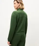 Campera deportiva Get Over color verde oscuro, confeccionada en mezcla de viscosa, poliéster y elastano. Cuenta con cuello alto, cierre frontal completo, bolsillos laterales, puños elásticos y cordón de ajuste en el bajo.