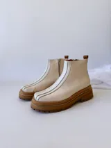 Botas Chelsea de cuero color crudo con elástico lateral, suela track color caramelo y tirador trasero de cuero con textura croco color marrón.