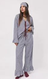 Conjunto de dos piezas de pijama confeccionado en algodón a cuadros vichy rosados y blancos. Incluye una camisa de manga larga con puños acampanados y cierre delantero con cordones para atar, y un pantalón largo de corte recto con volados en el ruedo.