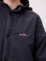 Campera reversible con capucha oculta, confeccionada en sarga de algodón con elastano en el exterior y nylon de poliéster en el interior. Presenta cierre frontal con botones a presión, costuras visibles en contraste y puños elásticos.