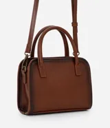 Cartera pequeña de mano con diseño estructurado, confeccionada en poliuretano color marrón con acabado envejecido. Cuenta con tapa frontal decorada con una hebilla metálica, cierre principal con cremallera, asa de mano rígida y correa larga ajustable y desmontable.