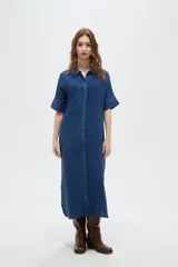 Túnica larga de viscosa azul, de corte holgado, con cuello camisero y cierre frontal de botones ocultos. Presenta mangas cortas con detalle de vuelta.