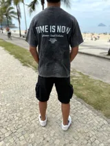 Remera oversize de color celeste melange, con diseño de estampado tipográfico en la espalda que incluye la frase "Time is Now" y otros detalles de colección.