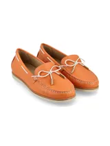 Mocasín de cuero naranja con textura granulada, detalle de lazo frontal blanco con punteras metálicas y costuras a la vista. Cuenta con suela plana de goma en tono crema.