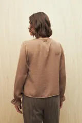 Camisa negra de manga larga con escote en V y botones forrados al tono en el frente. Destaca por su textura sutil y por el detalle de frunces con volados en la parte inferior.