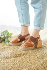 Sandalias de plataforma con taco cuadrado, confeccionadas en cuero con combinación de texturas lisa y grabada en tonos marrones. Presentan una tira ajustable con hebilla metálica en el tobillo.
