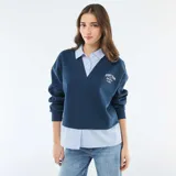Buzo azul de cuello en V con estampa frontal, que incorpora una camisa de rayas verticales celeste y blanca debajo, creando un efecto de capas.