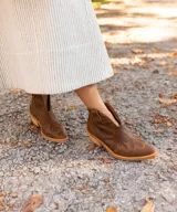 Botín de cuero vacuno color marrón oscuro, con taco de madera foliado en cuero de 5cm de altura, cierre lateral interno y horma de punta fina.