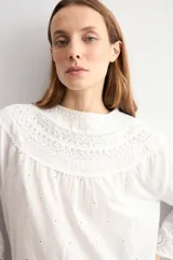 Blusa blanca de algodón con diseño de encaje bordado tipo broderie en el cuello, mangas y ruedo. Presenta mangas tres cuartos acampanadas y un corte holgado.
