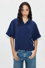 Camisa de cuello solapa y manga corta con dobladillo, presenta bolsillos de plastrón en el frente, bajo asimétrico y cierre frontal con botones ocultos.