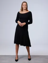 Vestido negro tejido de largo midi, con escote asimétrico adornado con tachas doradas, corte a la cintura y falda plisada. Marca Emma & Michele.